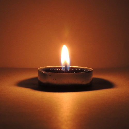 A candle burning in a candle holder surrounded by orange light